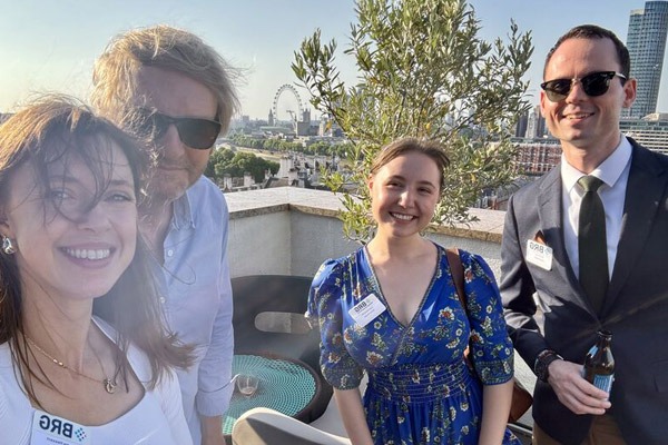Four people smile for a photo on a sunny rooftop overlooking a cityscape.