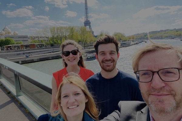 A selfie of four people with the Eiffel Tower in the background, taken on a sunny day.